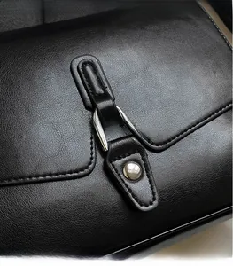 Detail of minimalist black leather crossbody bag featuring silver metal buckle and pebble grain texture