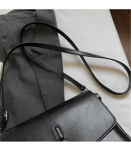 Detail of black faux leather crossbody bag with adjustable strap on suit background