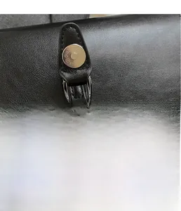 Detail of silver magnetic buckle and fine leather texture on a black crossbody bag