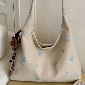 Cream shoulder bag with blue snowflake embroidery and wooden flower charm detail