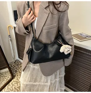 Detail of black pleated shoulder bag with a small side pocket and plush dog charm
