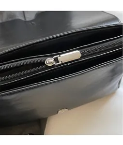 Detail of silver metallic zipper puller and internal pocket of black leather crossbody bag