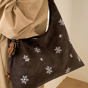 Brown suede tote bag with snowflake embroidery and floral charm shown on shoulder