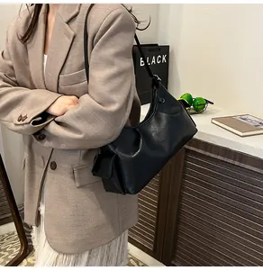 Detail of black pleated shoulder bag with side pocket shown on a brown blazer outfit