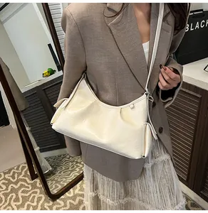 Detail of a creamy white crescent bag with pleats and adjustable strap on a model