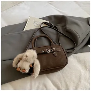Detail of dark brown matte leather bag with buckle strap and a plush rabbit pendant