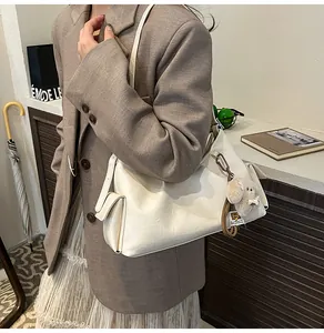Detail of cream pleated shoulder bag featuring a brown plush puppy charm on a side pocket