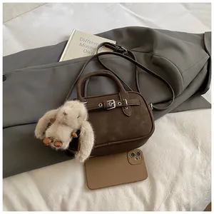 Detail of dark brown leather handbag with silver buckle, plush bunny, and matching phone case