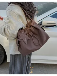 Dettaglio borsa a secchiello in pelle marrone scuro con coulisse e ciondolo a stella in strada