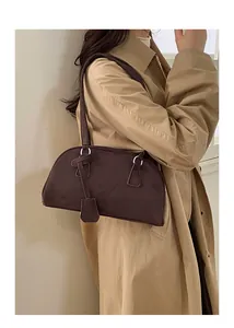 Brown suede bowling bag styled as a shoulder bag on a model wearing a beige coat