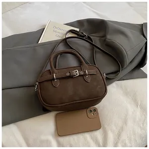 Detail of vintage brown crossbody bag with strap and buckle accent next to a smartphone