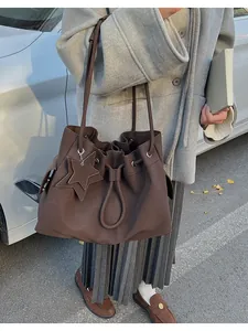 Dettaglio di una grande borsa tote marrone con ciondolo a stella, portata da una modella