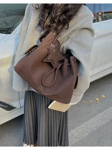 Dettaglio di una borsa a secchiello marrone scuro con ciondolo a stella sulla spalla