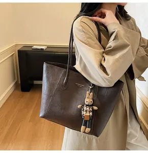 Close-up of a deep brown tote bag with slim handles and a small bunny charm on a model
