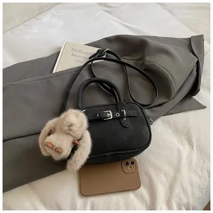 Detail of black leather crossbody bag with silver buckle and plush bunny charm accessory