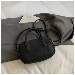 Detail view of the black matte suede handbag with round handles and adjustable strap