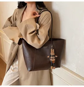 Detail of dark brown tote bag with gold logo and cute rabbit charm on beige trench coat