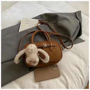 Close-up of brown square bag with metal buckle, shoulder strap, and white plush bunny charm