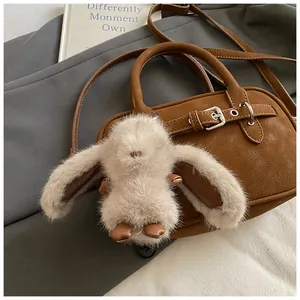 Detail of cute beige plush bunny keychain charm on a brown pebbled leather bag with metal clasp