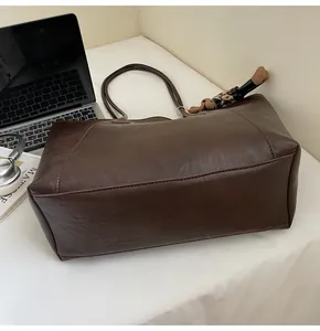 Macro shot of large dark brown tote bag on white fabric with laptop and book detail
