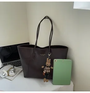 Close-up of dark brown matte leather tote bag with a cute rabbit charm and laptop