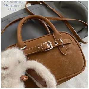 Close-up of brown lychee leather handbag with silver buckle and plush bunny charm