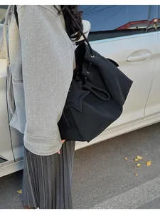 Dettaglio della borsa a secchiello in pelle nera con coulisse e toppa a stella su modella