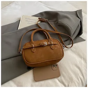 Detail of a caramel leather mini square bag showing the decorative strap buckle and hand strap