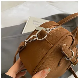Detail shot of brown lychee leather texture and silver hardware on a round crossbody bag