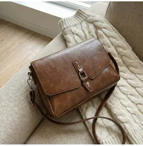 Detail of vintage brown leather crossbody bag featuring silver hardware on a cozy sofa