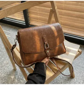 Detail view of brown vintage PU leather crossbody bag with silver hardware on a chair