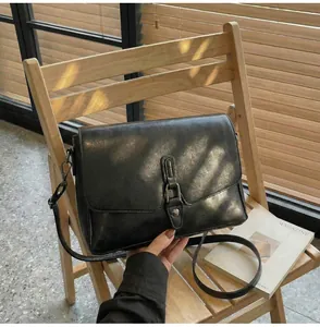 Retro black leather shoulder bag detail with silver buckle on a wooden chair