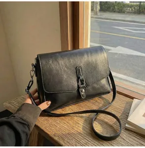 Detail view of the black crossbody bag showing its glossy synthetic leather and silver rivets