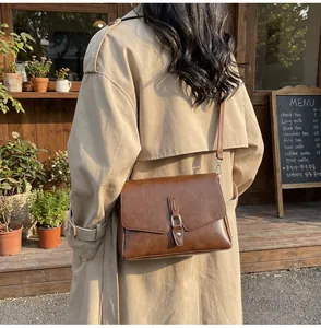 Close-up of brown leather crossbody bag with metal buckle in a warm cafe setting