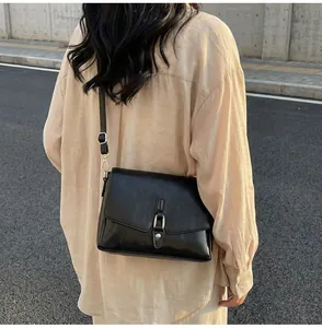 Detail of a black leather crossbody bag with silver metal buckle and adjustable shoulder strap