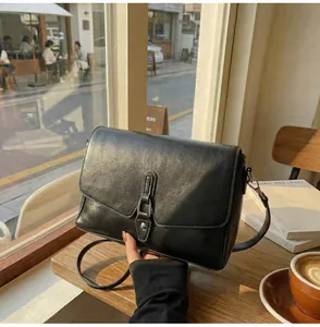Close-up of minimalist black leather crossbody bag with metal buckle on a cafe table