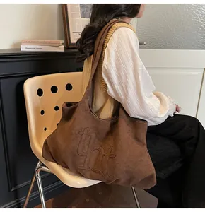 Groot aanzicht van donkerbruine suède tote bag met reliëf tht-logo op de tas