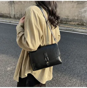 Outdoor shot of minimalist black leather crossbody bag with silver buckle on a model