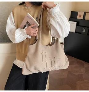 Detail van de kaki suède draagtas met reliëfletters op een casual lifestyle-model