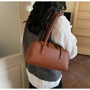 Dettaglio della borsa bowling in pelle marrone con cuciture bianche e texture fine