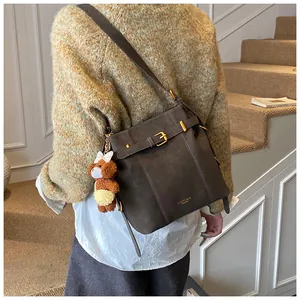 Detail der braunen Wildleder-Beuteltasche mit Metallschnalle und süßem Bärenanhänger
