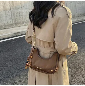 Detail showing deep brown faux leather half-moon bag with gold chain and wooden bead charm