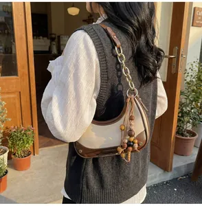 Detail of contrast color half-moon bag with metal chain and beaded tassel charm