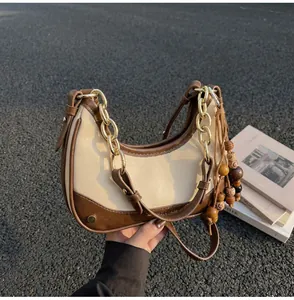 Detail view of contrast leather half-moon bag with gold chain and wooden bead tassel
