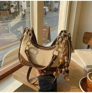 Detail of contrast leather shoulder bag featuring wood bead tassel and gold chain strap
