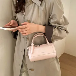 Sac Boston rose en cuir ciré avec bandoulière chaîne argentée porté sur manteau beige