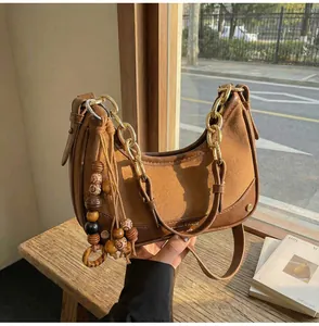 Detail view of leather crossbody bag with chunky gold chain and wooden bead tassel decor