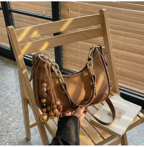 Detail of a brown half-moon shoulder bag with gold chain and wooden bead tassel