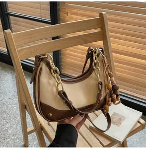 Detail of a chic cream and brown crescent bag featuring a boho bead tassel on a wooden chair