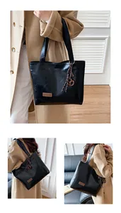 Détail de sac cabas en cuir PU noir montrant le pendentif tressé et le logo de mode
